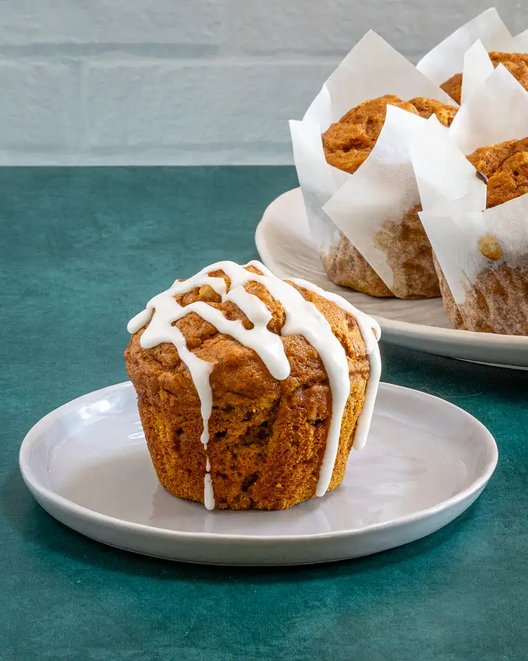 Golden brown muffin topped with white icing on a small white plate.