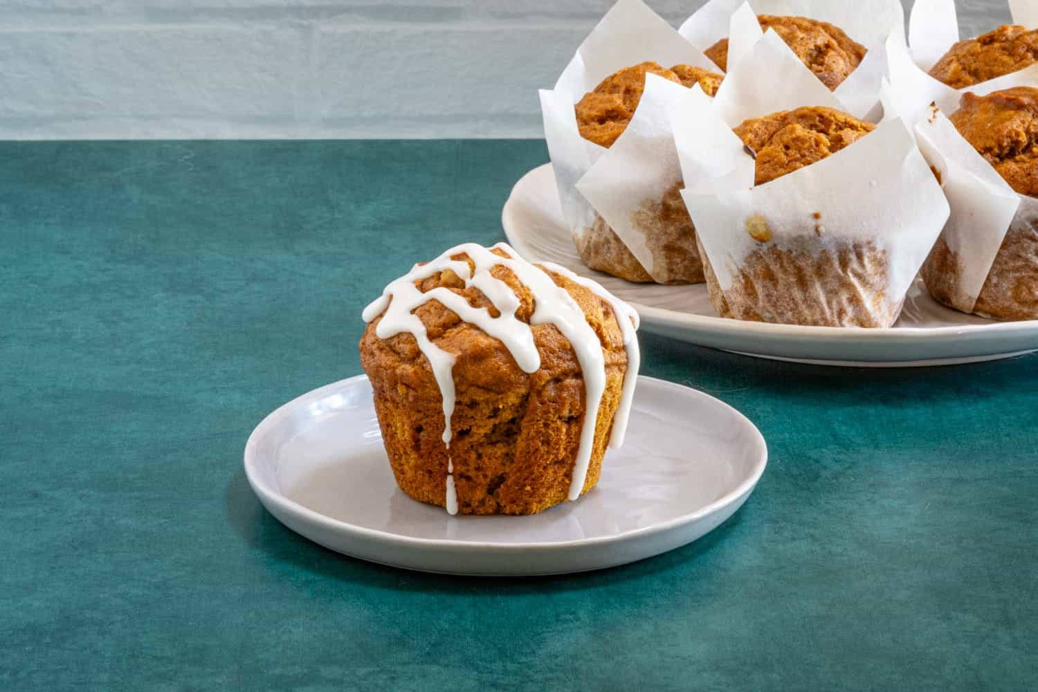 Iced pumpkin muffin on a plate with more muffins in the background.
