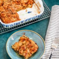 A baked French toast casserole serving with maple syrup and the casserole dish in the background.
