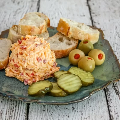 Cream cheese salad with bread, pickles, and olives on a ceramic plate.