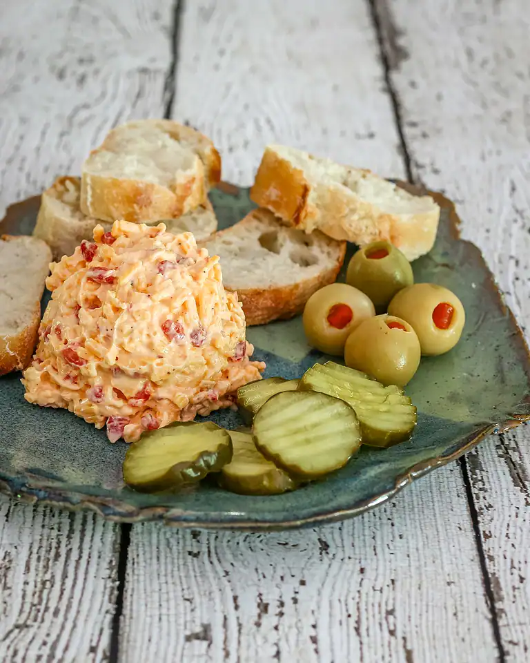 Cream cheese salad with bread, pickles, and olives on a ceramic plate.