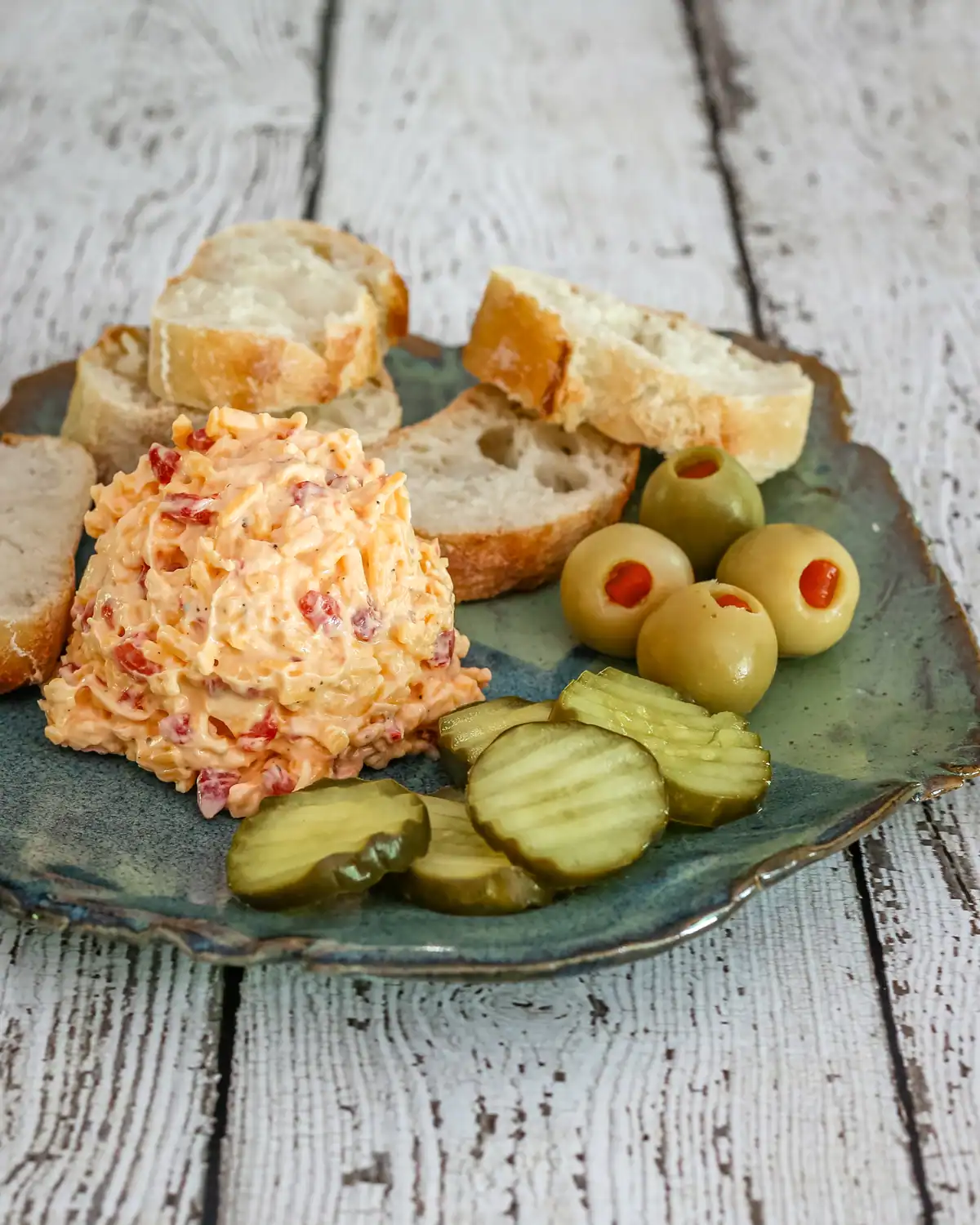 Cream cheese salad with bread, pickles, and olives on a ceramic plate.
