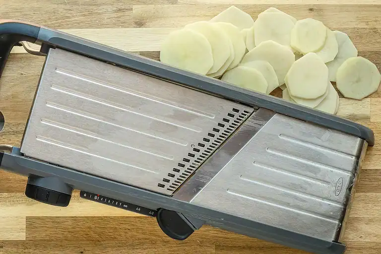 Grid-style potato slicer with sliced potatoes on wooden surface.