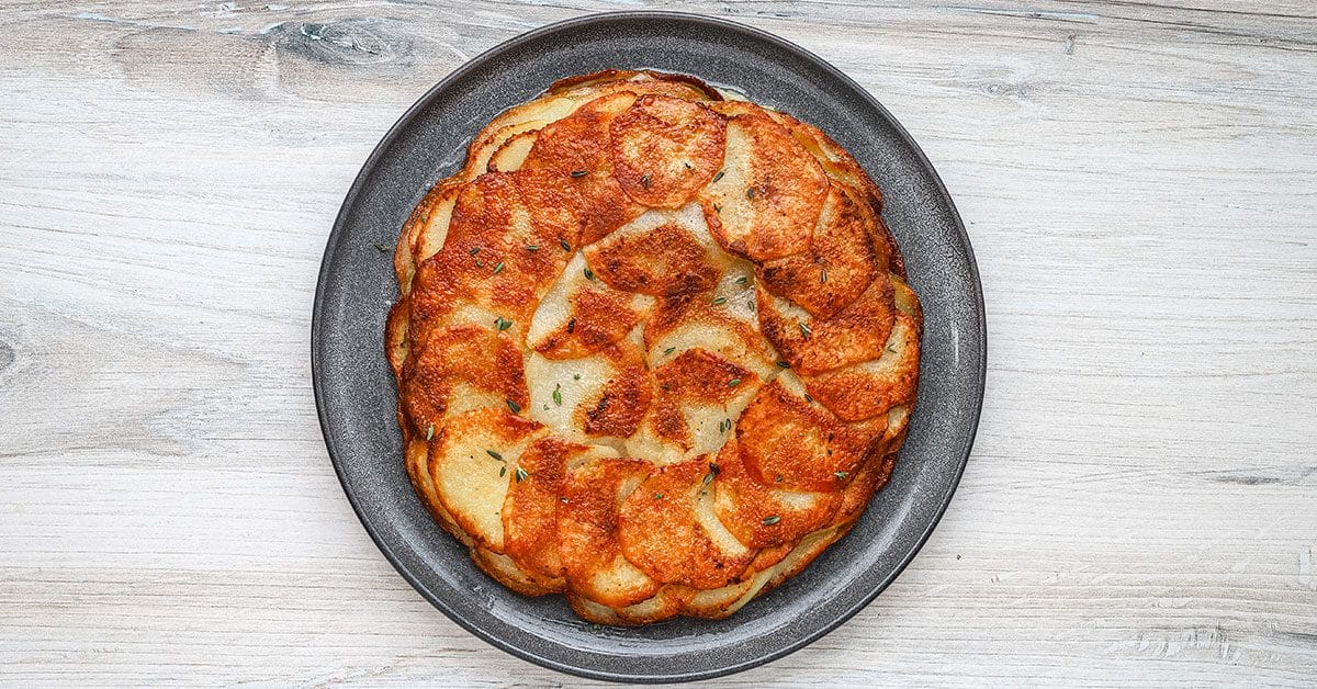 A plate with pommes Anna, golden brown and garnished with thyme.