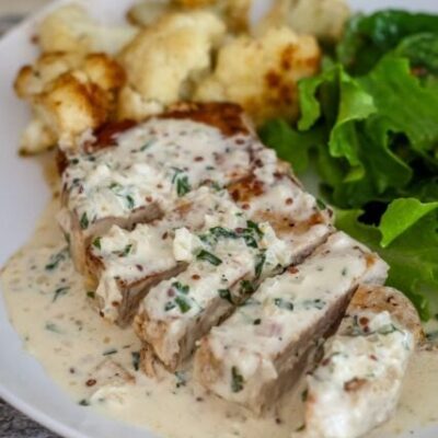 pork chops with mustard cream sauce on a plate with cauliflower and salad