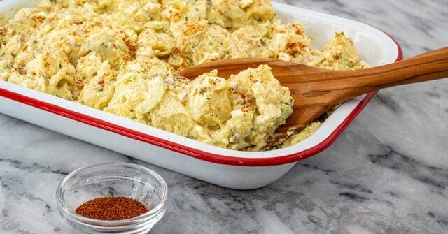 A serving dish with potato and egg salad with mayo and mustard dressing.