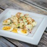 A tangy, delicious potato salad on a plate with bacon and eggs.