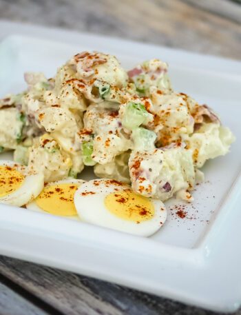 A bacon and egg potato salad on a serving plate with some sliced hard-boiled eggs on the side.