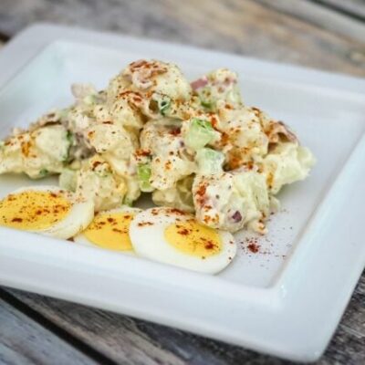 A bacon and egg potato salad on a serving plate with some sliced hard-boiled eggs on the side.