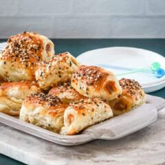 A serving tray with baked puff pastry pigs in a blanket with small appetizer plates and picks for serving.