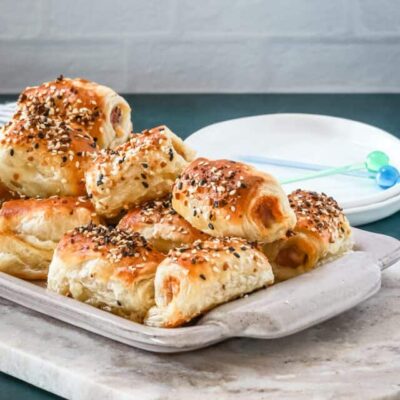 A serving tray with baked puff pastry pigs in a blanket with small appetizer plates and picks for serving.
