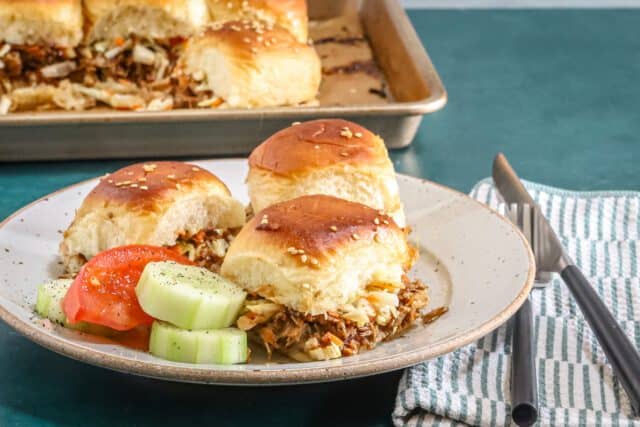 Savory pulled meat sliders with fresh cucumber and tomato slices.