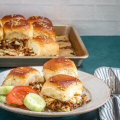 Steamed buns filled with shredded meat and vegetables, served with cucumber and tomato slices.