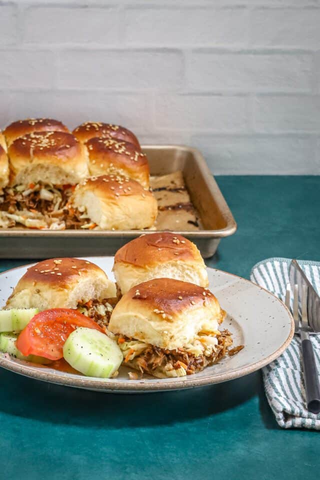 Steamed buns filled with shredded meat and vegetables, served with cucumber and tomato slices.