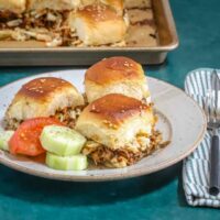 Bowl of fluffy pulled pork sliders with fresh cucumber and tomato slices.