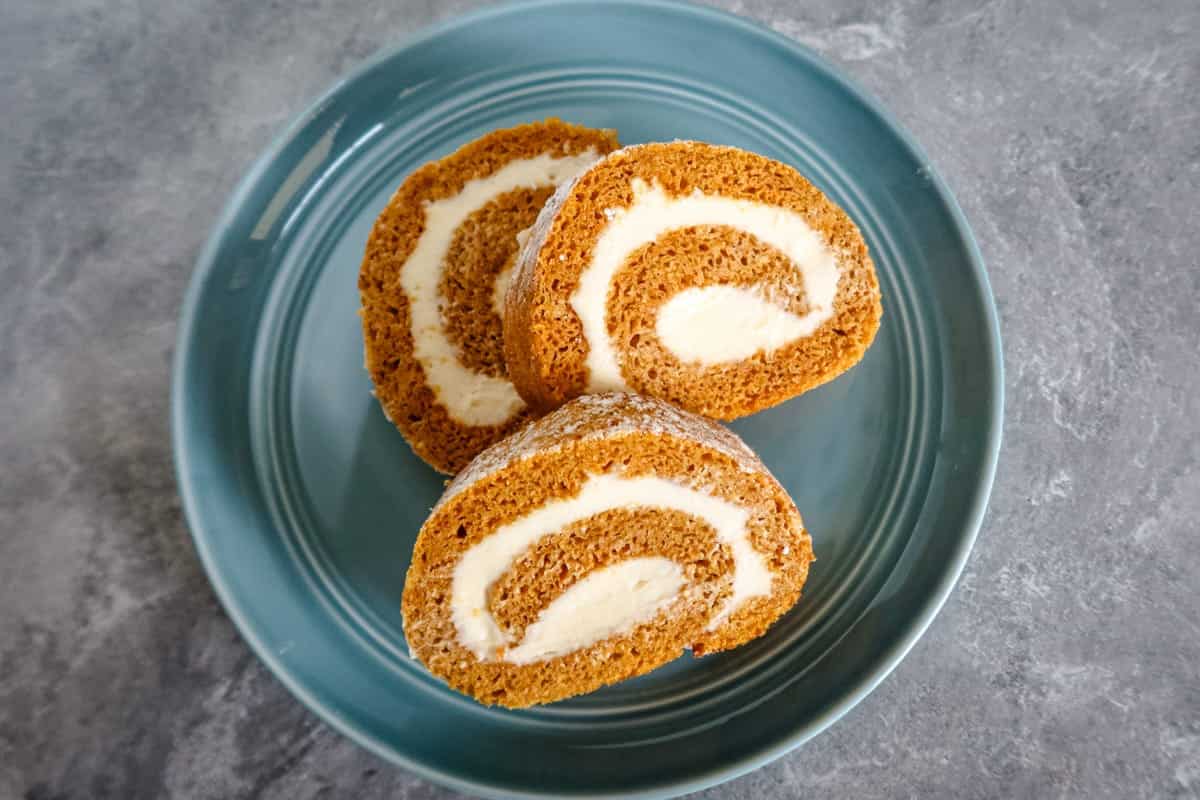 A pumpkin cake roll with cream cheese filling on a teal plate.
