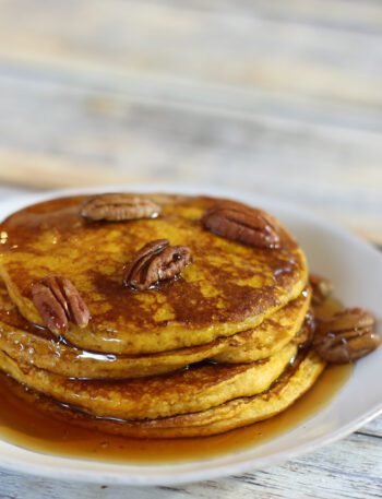A stack of pumpkin pancakes with toasted pecans and syrup.