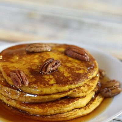 A stack of pumpkin pancakes with toasted pecans and syrup.