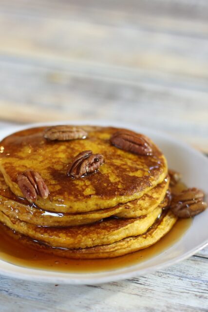 A stack of pumpkin pancakes with toasted pecans and syrup.