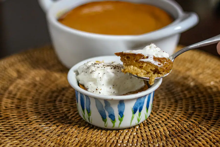 Pumpkin pudding topped with whipped cream, spooned out of a small ramekin.