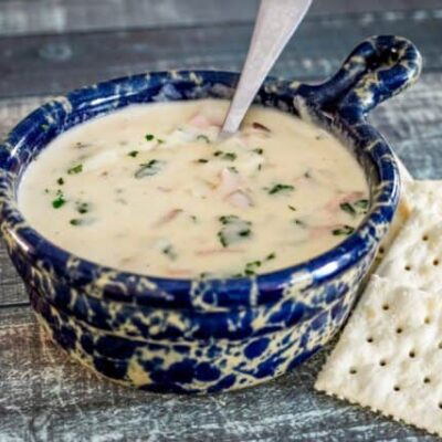 A bowl of potato soup with crackers on the side.