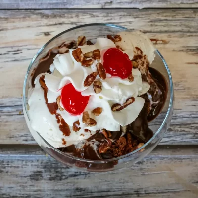 Rich chocolate ice cream topped with whipped cream, cherries, and chopped nuts in a glass dish.