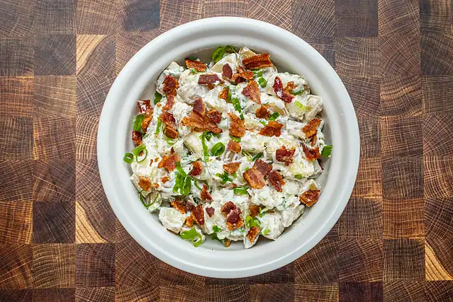 Ranch potato salad ingredients combined with some cooked crumbled bacon in a serving bowl.