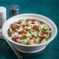 Creamy chicken salad with bacon and green onions in a white bowl.