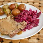 A dinner plate with braised red cabbage, pork chop, and potatoes