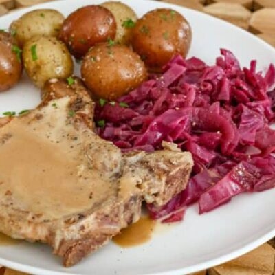 braised red cabbage is shown with a pork chop and baby potatoes on a plate