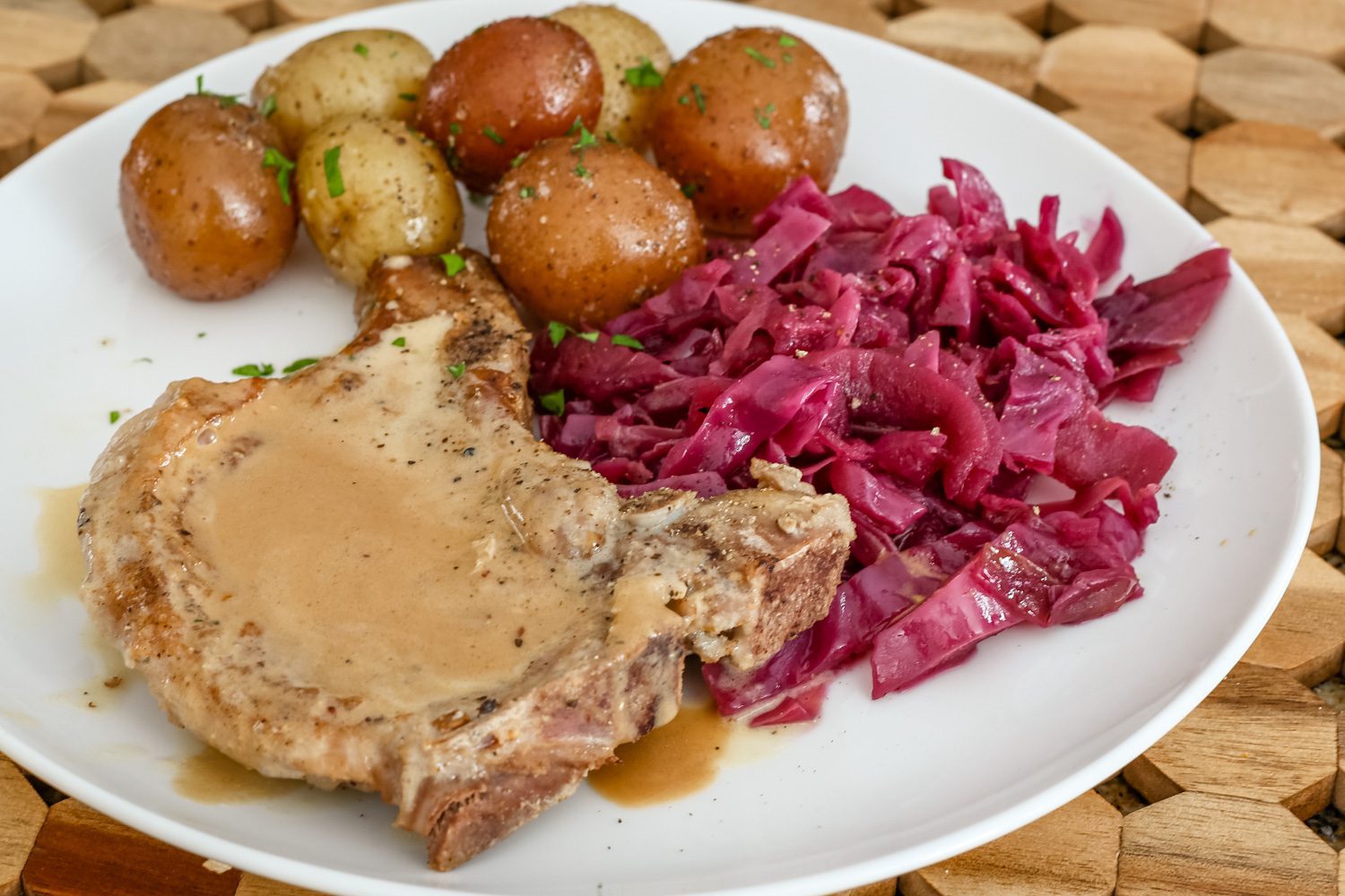 braised red cabbage is shown with a pork chop and baby potatoes on a plate