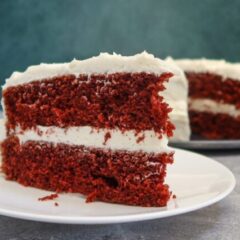red velvet cake slice on a plate with the larger cake in the background
