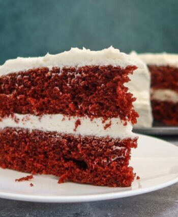 red velvet cake slice on a plate with the larger cake in the background