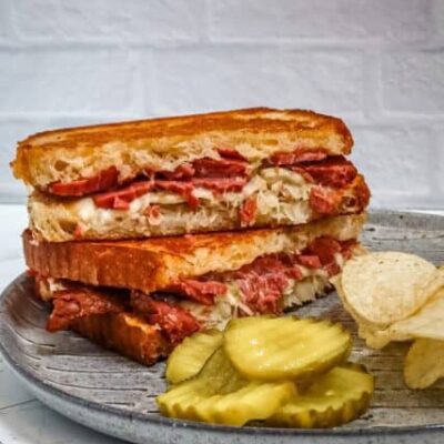 reuben sandwich on a plate with chips and pickles