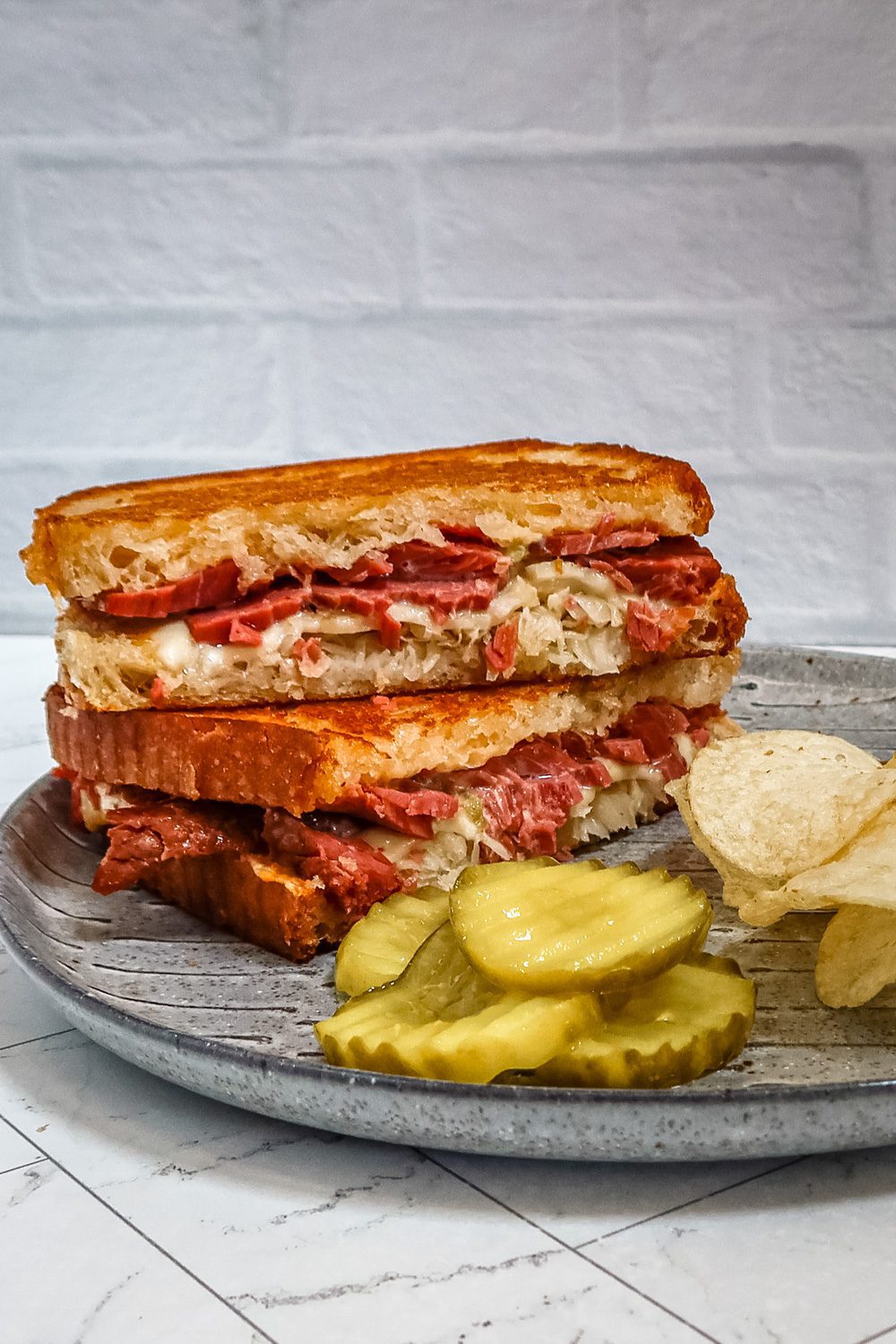 reuben sandwich on a plate with chips and pickles