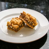Chocolate chip cookie bars with nuts on a white plate.