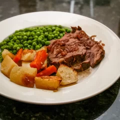 Roast beef with vegetables and green peas on white plate.