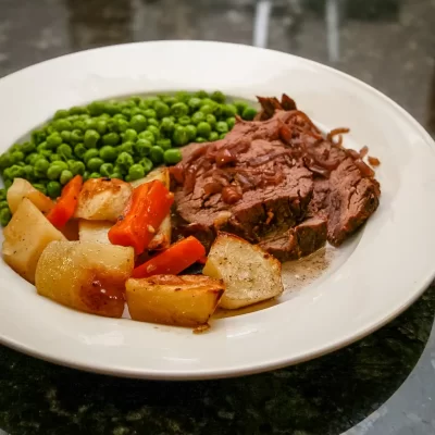 Roast beef with vegetables and green peas on white plate.