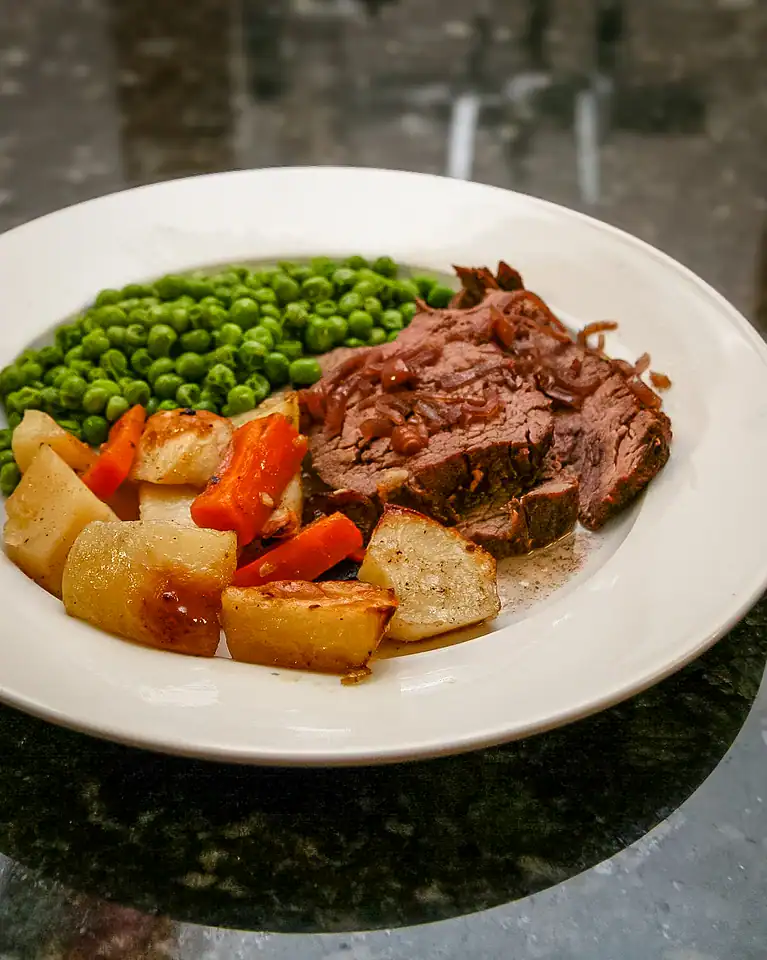 Roast beef with vegetables and green peas on white plate.