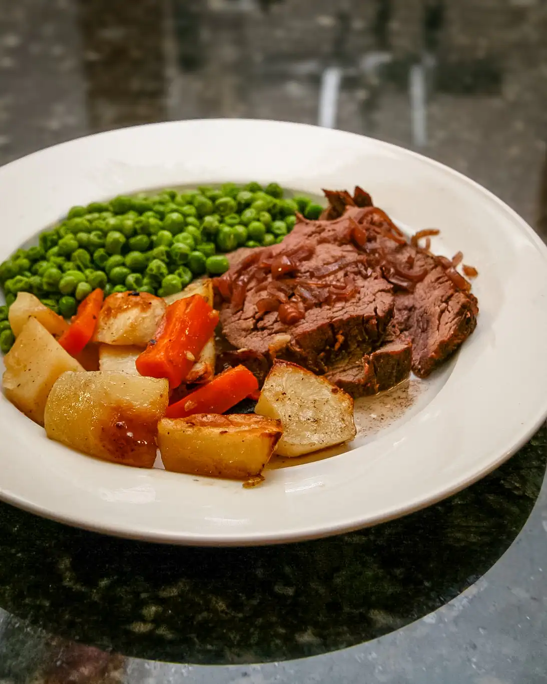 Roast beef with vegetables and green peas on white plate.