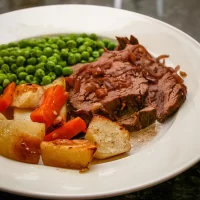Roast beef with vegetables and peas on a white plate.