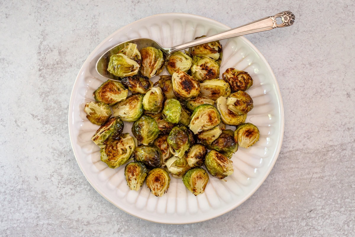 A plate of roasted brussels sprouts with a serving spoon.