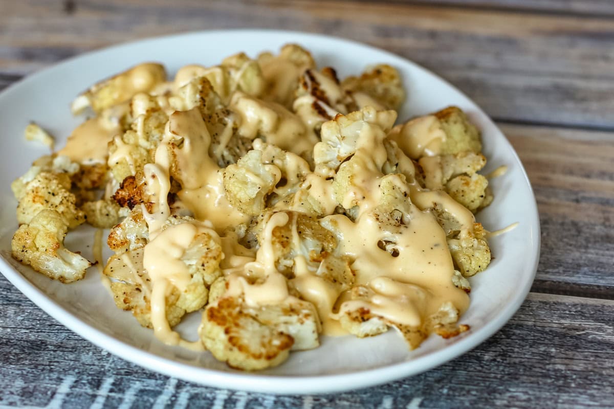 Roasted cauliflower on a serving platter with a drizzle of cheese sauce.
