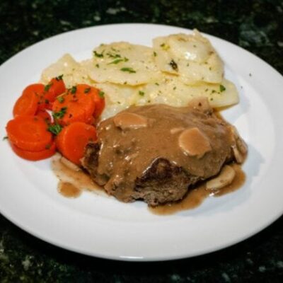 salisbury steaks on a plate with scalloped potatoes and carrots