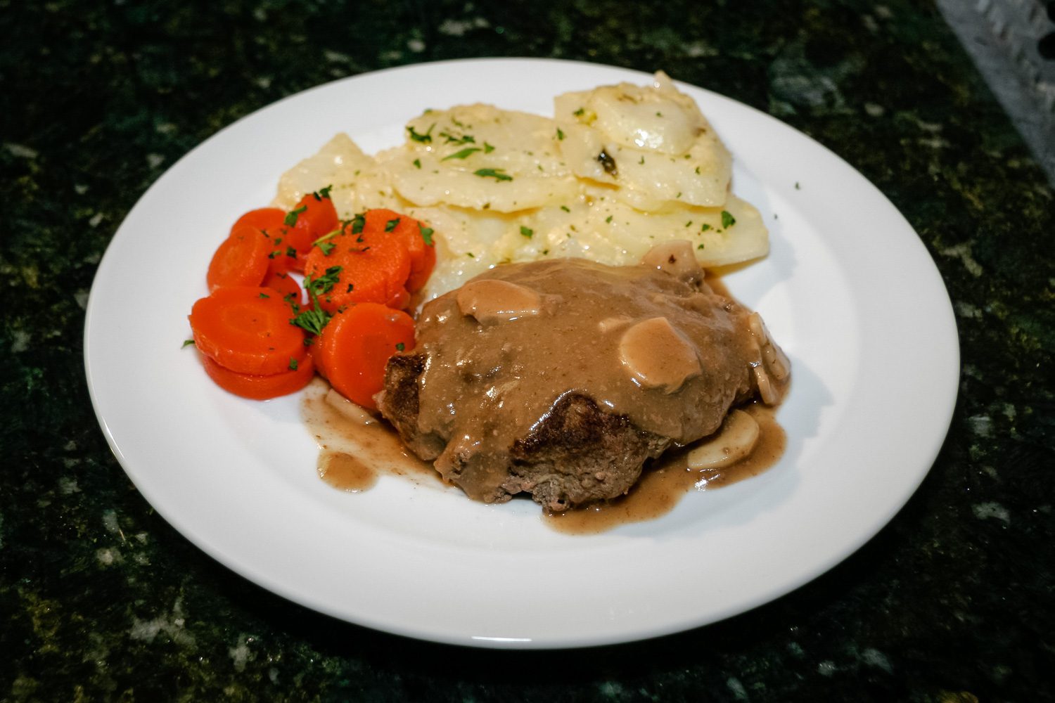 salisbury steaks on a plate with scalloped potatoes and carrots