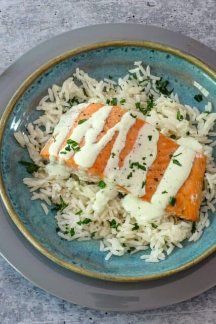 a salmon fillet on a bed of rice with a drizzle of basil mayonnaise.