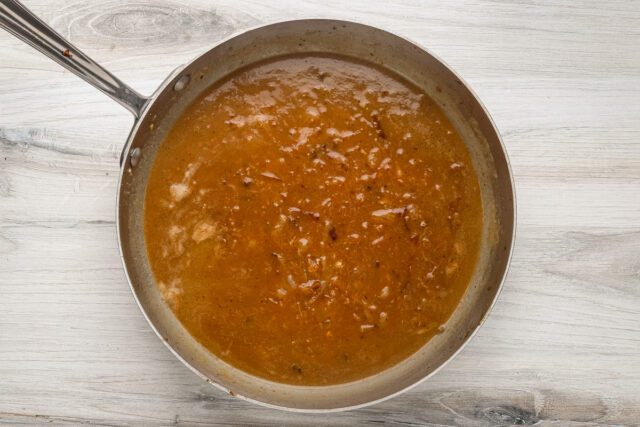 Sauce made with chicken broth and onions is simmering for smothered pork chops.