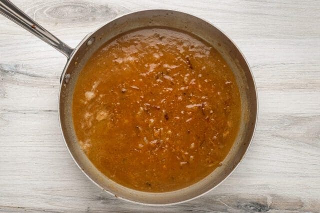 Savory soup simmering in a silver pan on a white wooden surface.