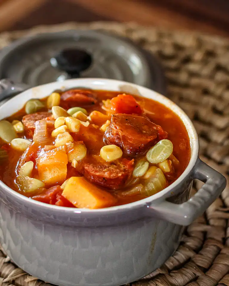 Succulent stew with chunks of sausage, vegetables, and corn in a ceramic bowl.