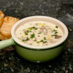 a bowl of corn chowder with crumbled cooked sausage and cheese